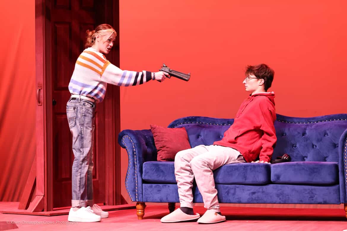 actors threatens another with a gun, red cyc lighting